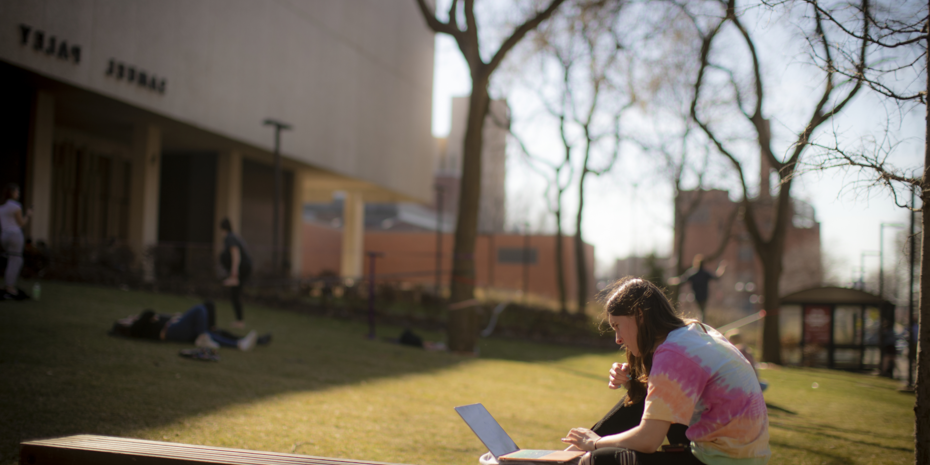 A Temple student working on their laptop while sitting on a bench outside Paley Hall.