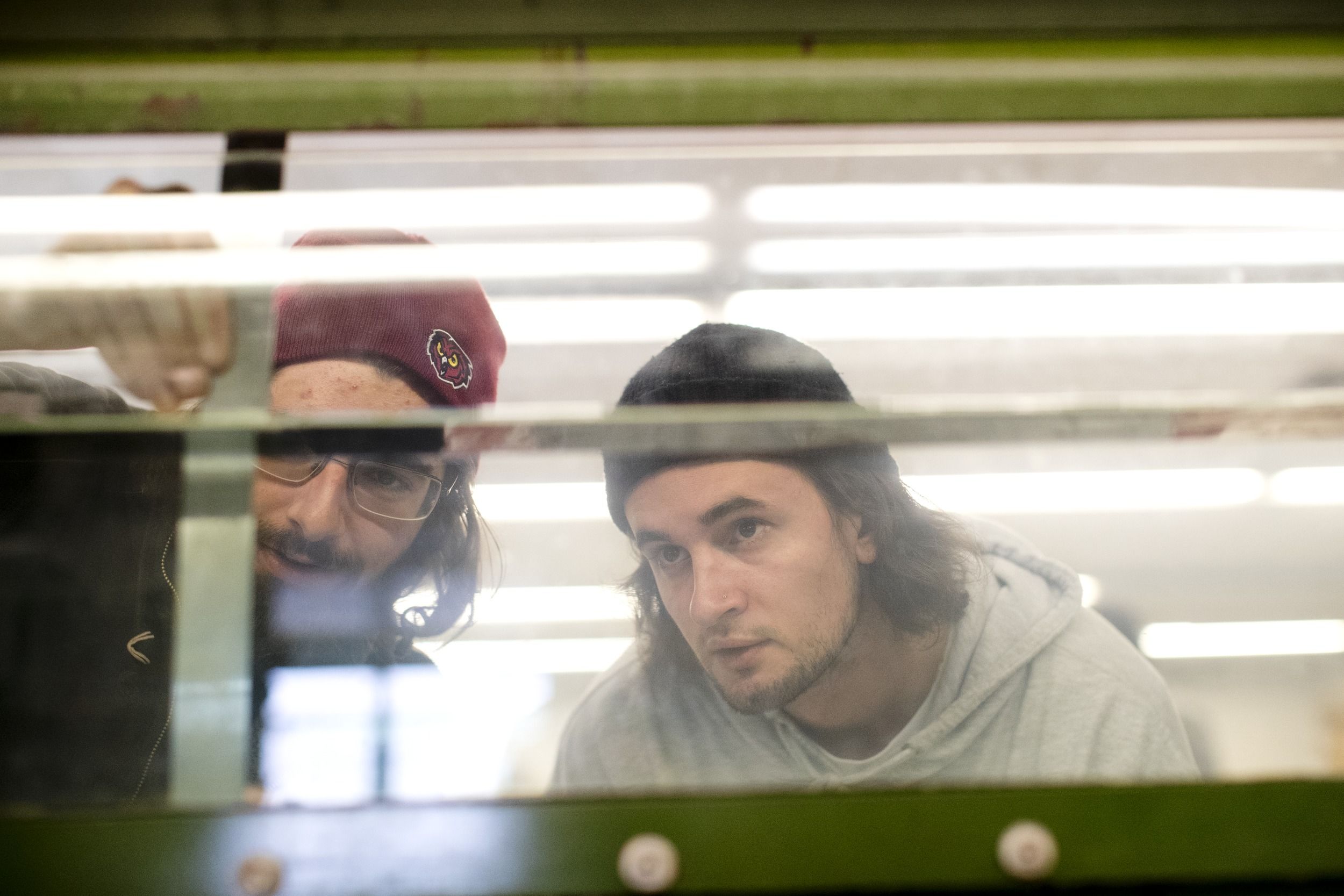 Two engineering students are looking at something through a glass panel.