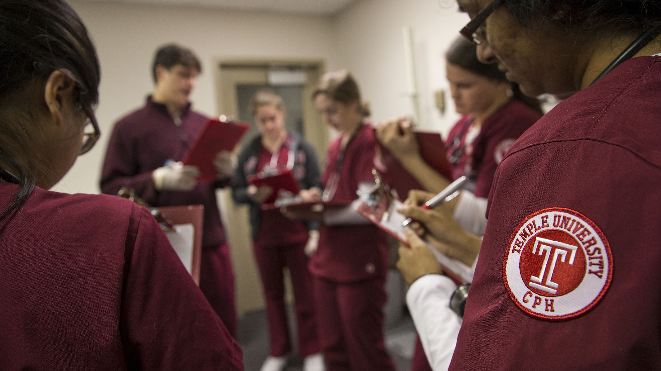 A group of nursing students are gathered in a circle and writing on clipboards.