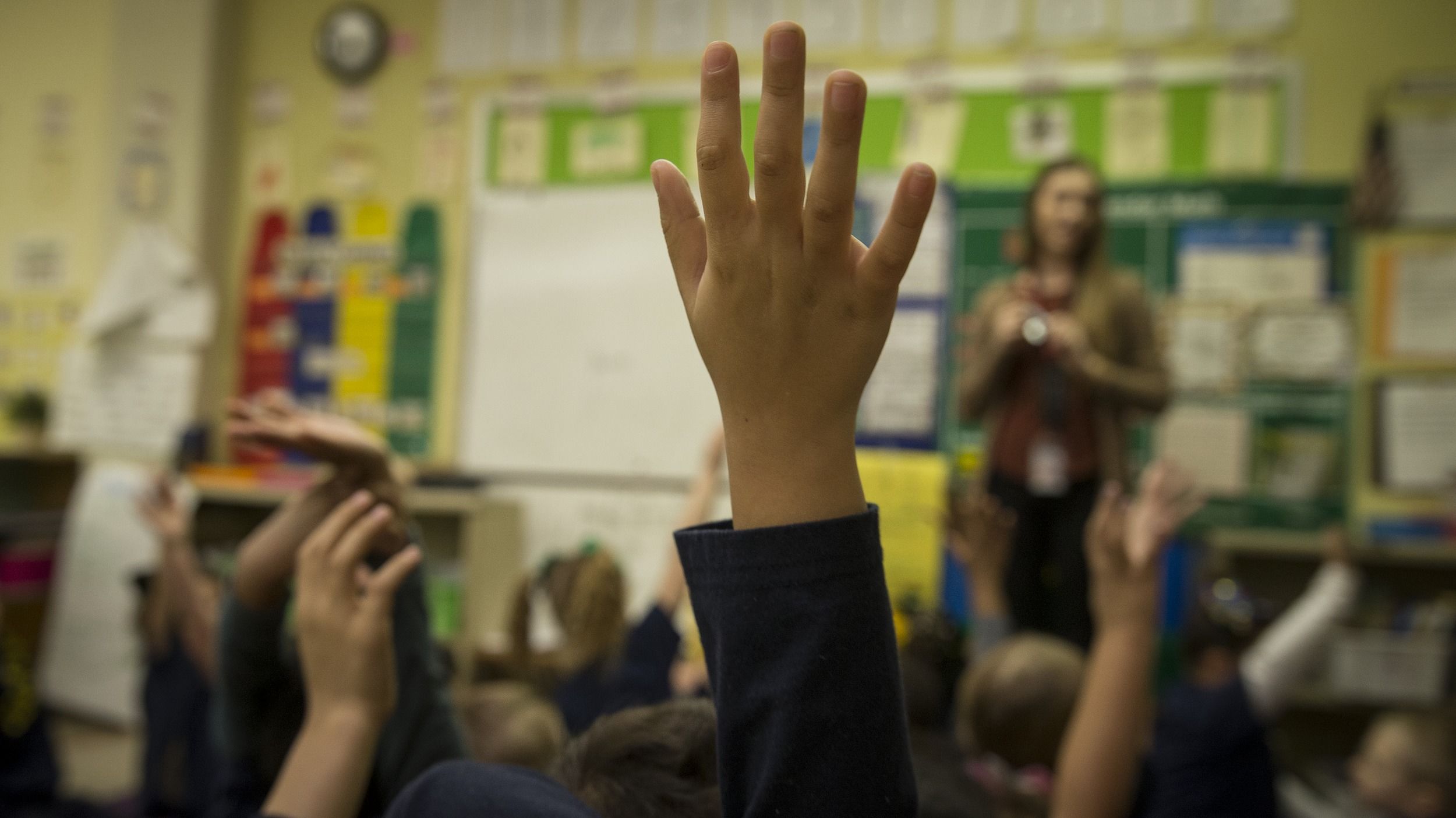 A close-up of a student's hand raised in an elementary classroom.