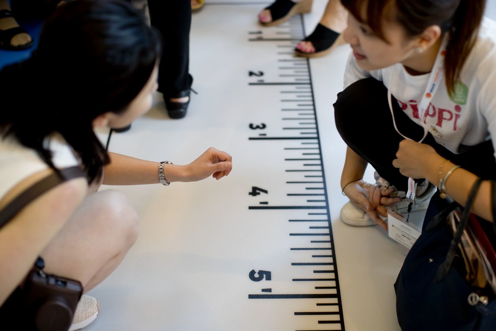 Two students crouch down in front of a giant measuring tape.