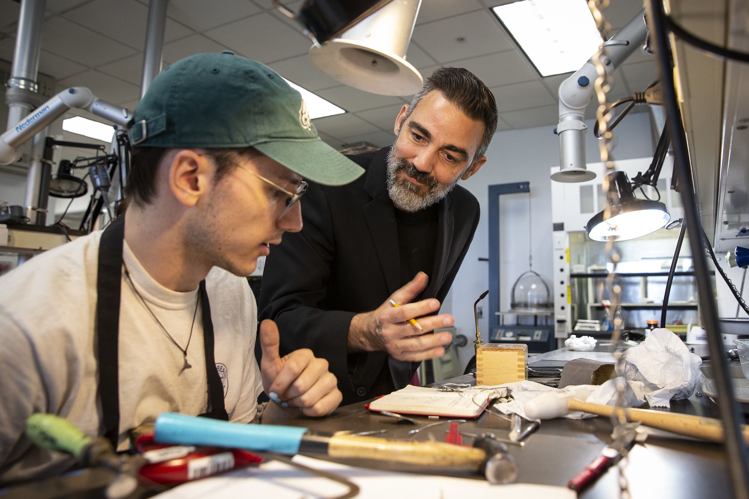 A Temple professor assists a student in creating metal jewelry.