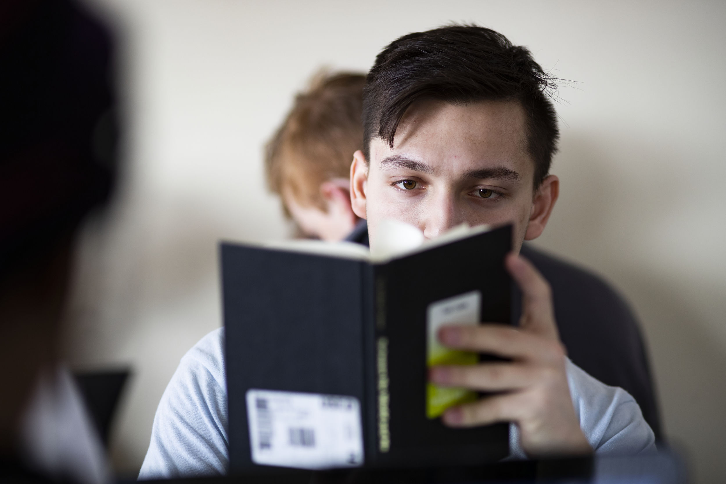 A student sits at his desk while reading a book.