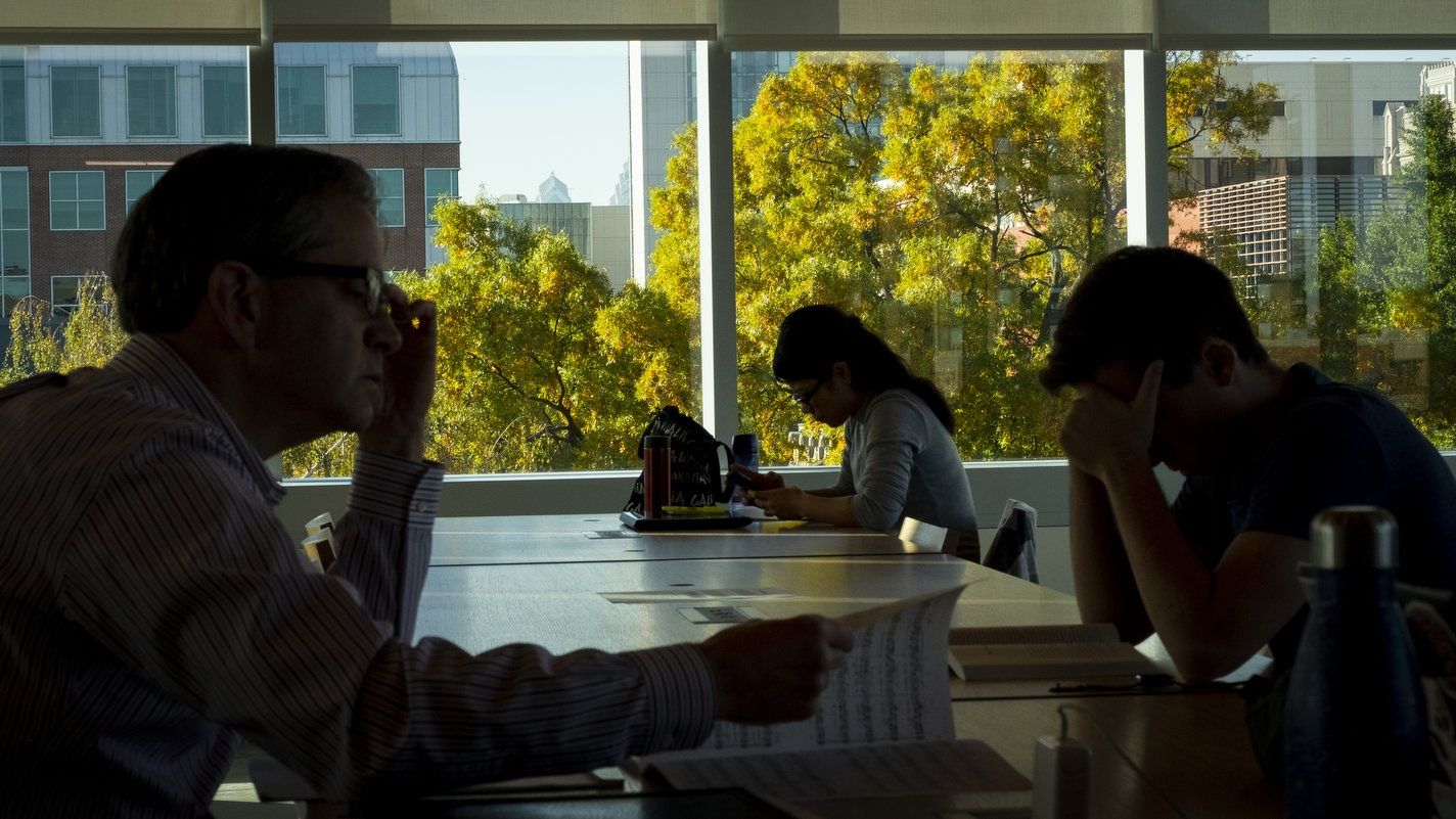 Silhouettes of students working at tables. A window overlooks Main Campus.