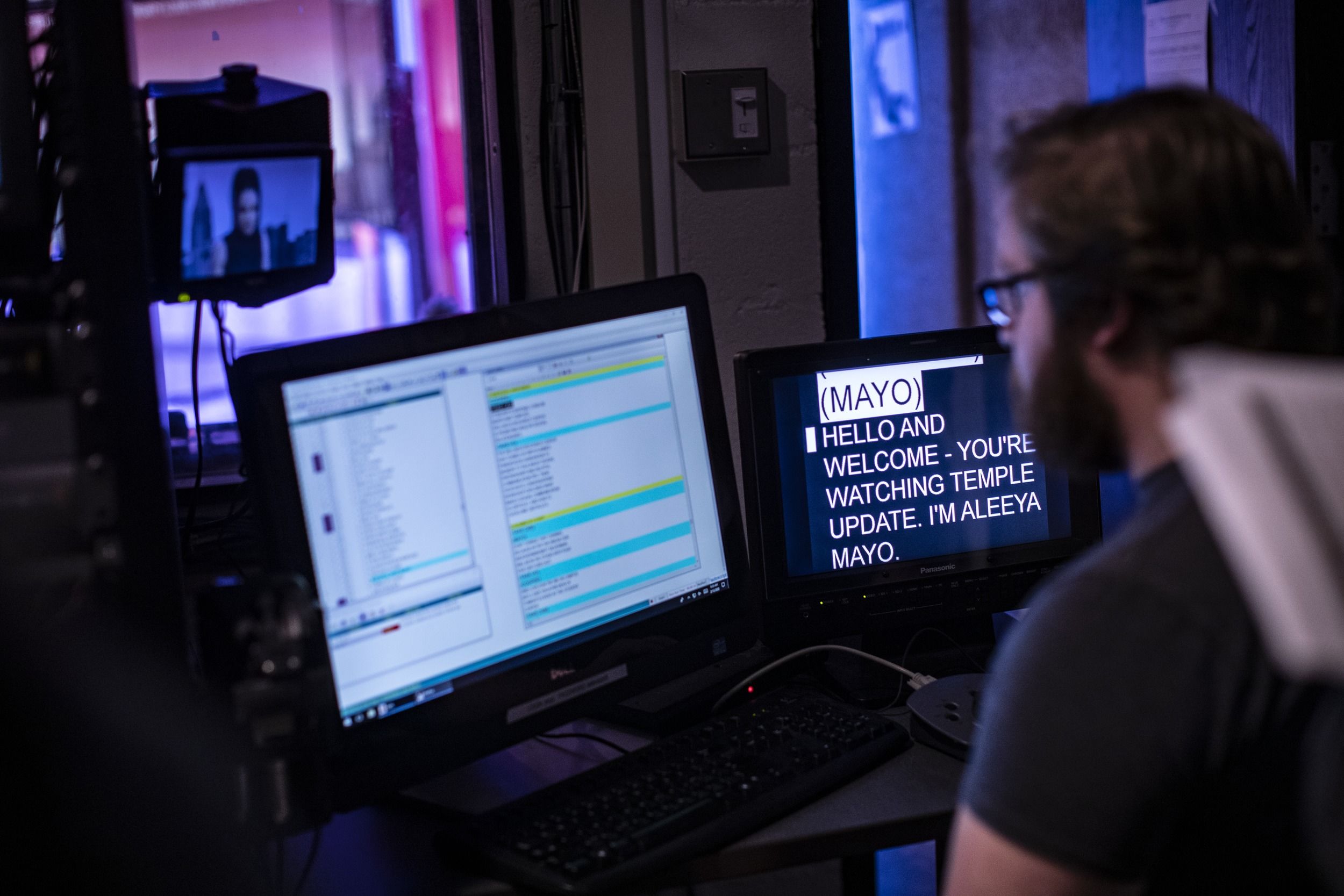 A student sits in front of two monitors in a dark broadcasting studio.