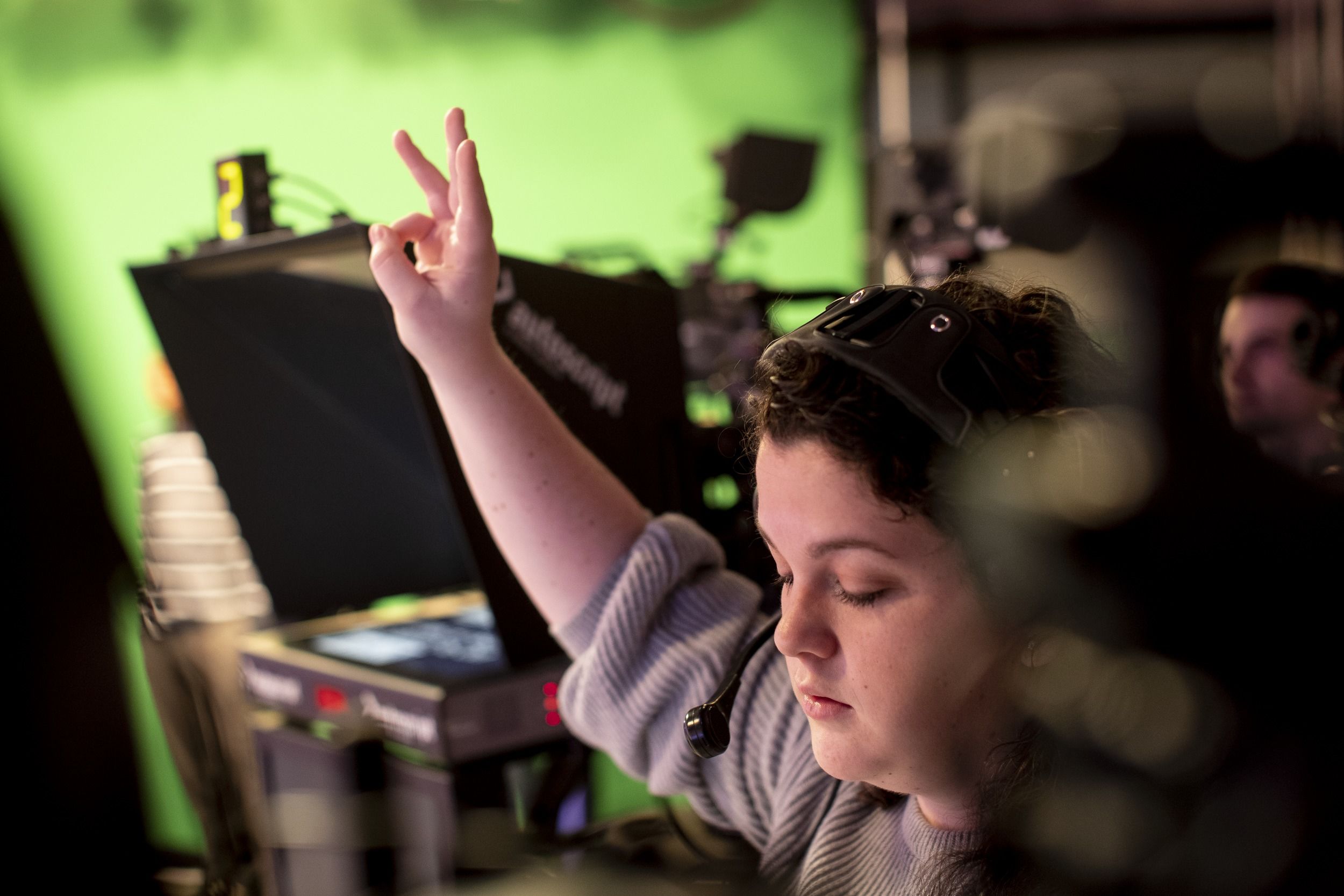 A student with three fingers raised in the air to let people know when to begin shooting in a broadcasting studio.