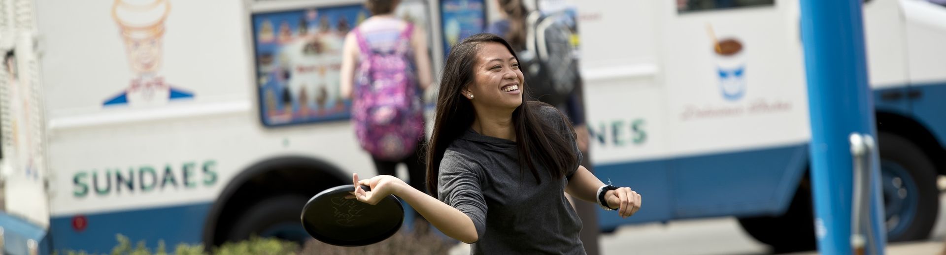 A student laughing and smiling while playing frisbee outside on Main Campus.