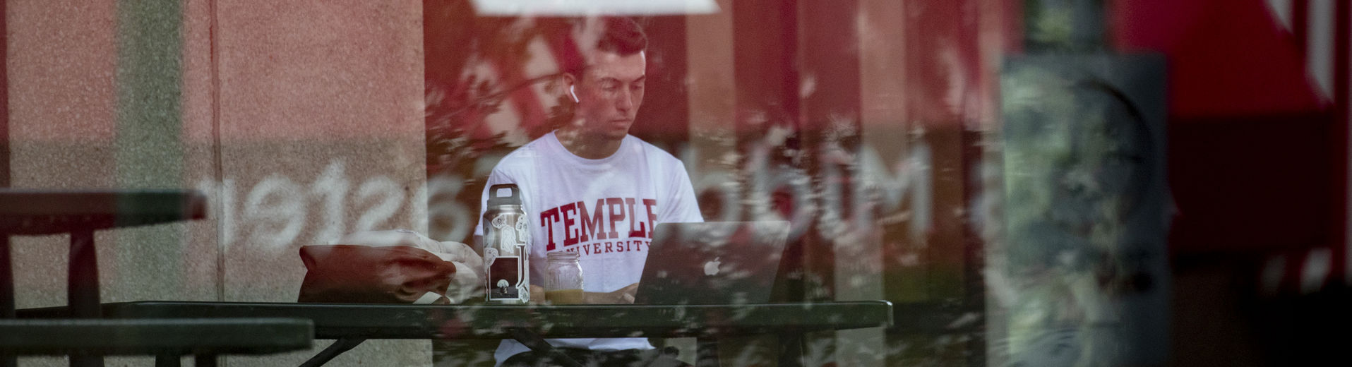 A student working on a laptop while sitting outside on Temple’s Main Campus.